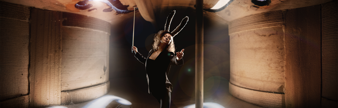 Woman dressed in a suit and rabbit ears holding a bow aloft, pictured inside a cello.