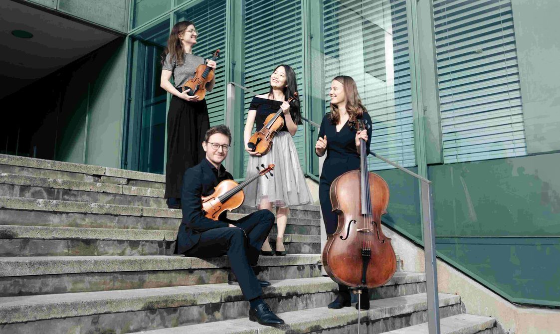 Aventurin Quartet, three men and one woman sitting and standing on a set of steps holding their string instruments and smiling.