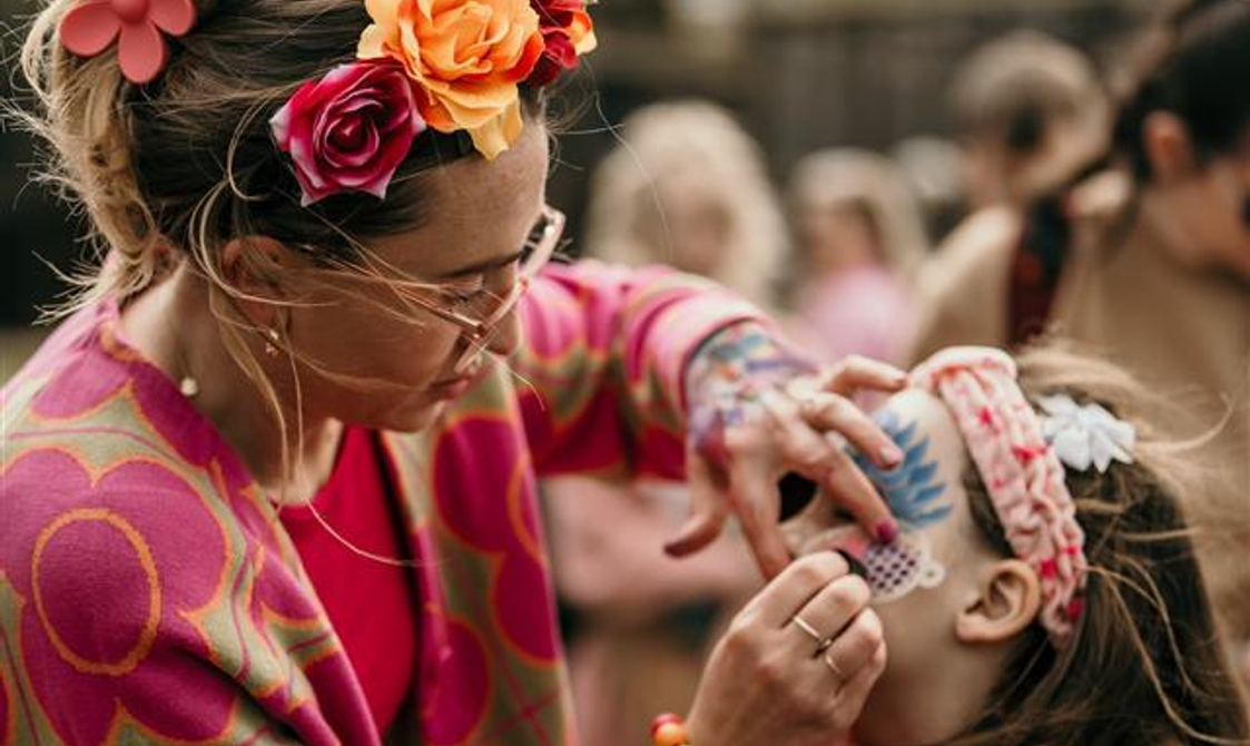 Woman with flowers in her hair painting a butterfly on a child's face.
