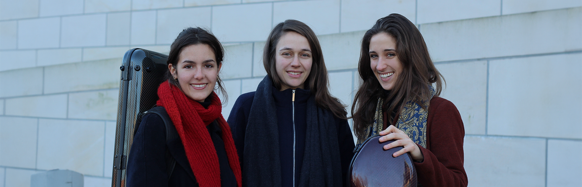 Three women from Trio Brontë standing together outside, holding their instrument cases and smiling.