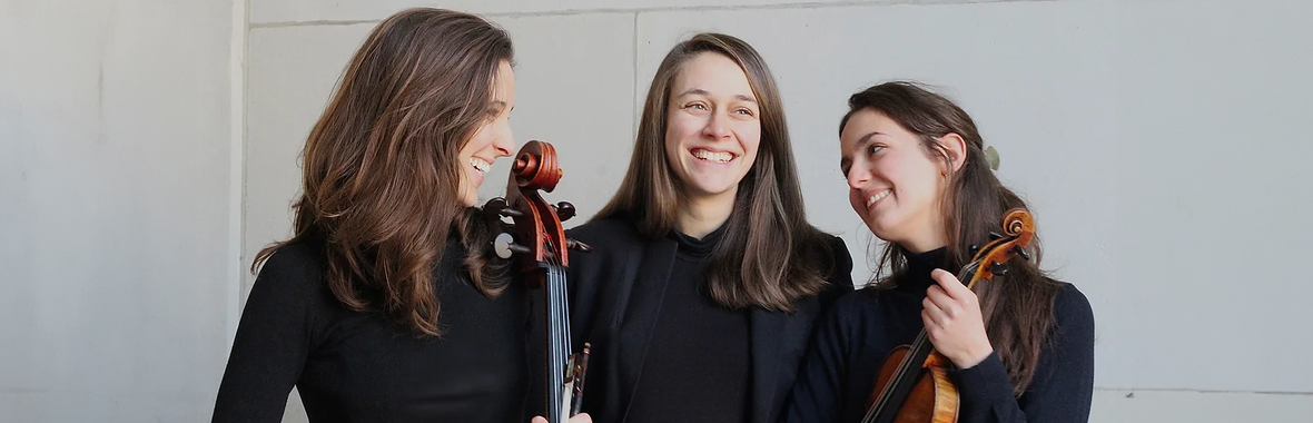 Three women from Trio Brontë wearing black, standing together with their instruments and smiling.