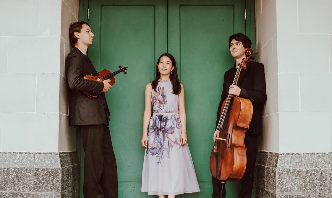 Trio Kagura, two men and a woman standing in a green doorway.