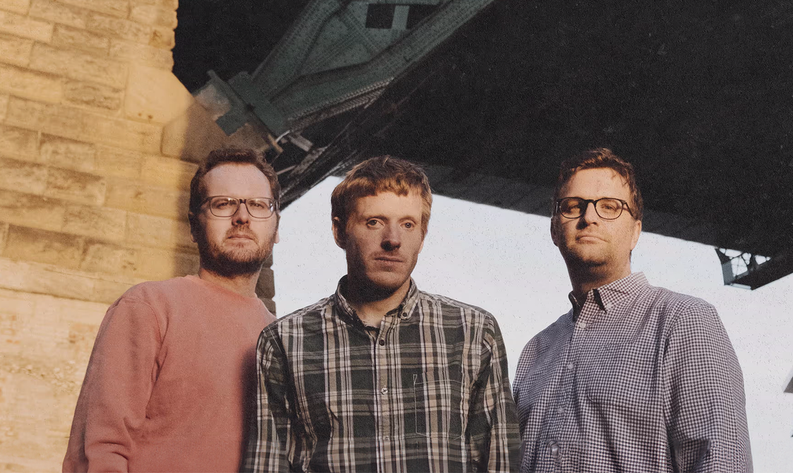 Three men standing together under a bridge.