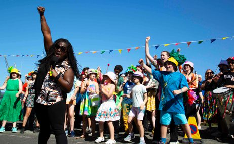 A group of Aldeburgh Young Musicians in colourful outfits fist pumping the air with Hannabiell Sanders.