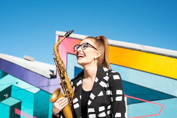 Jess Gillam holding a saxaphone against a colourful background.