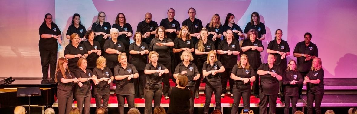 A choir of people singing lit by purple lights.