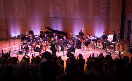 Aldeburgh Young Musicians standing and sitting onstage, playing their instruments.