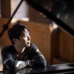 George Xiaoyuan Fu leaning against a piano, looking into the distance.