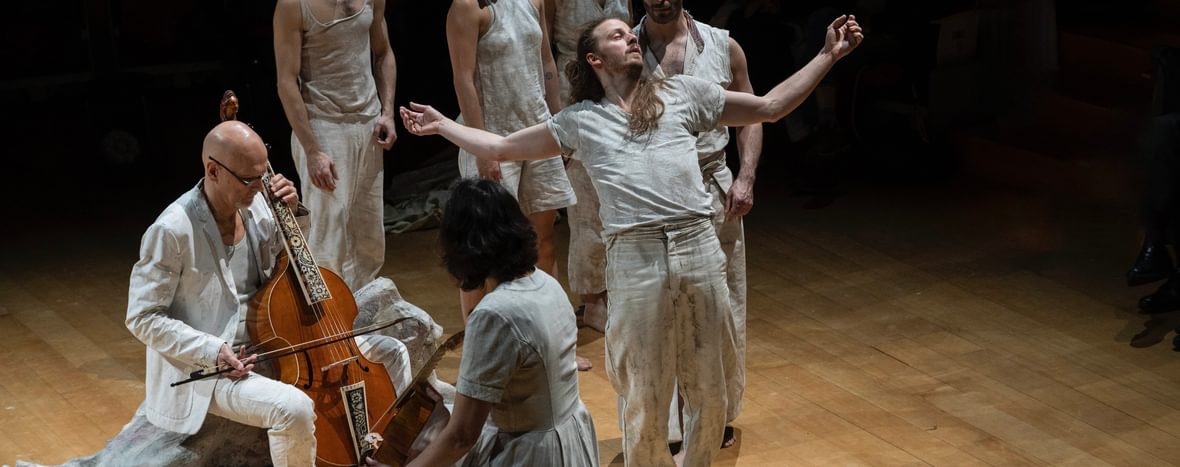 Dancers and musicians dressed in white. One of them has their arms held out.