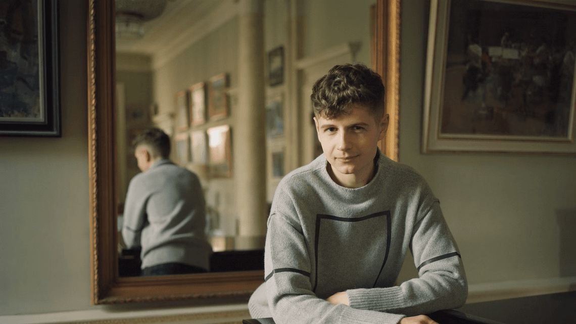 Pavel Kolesnikov leaning on a piano.