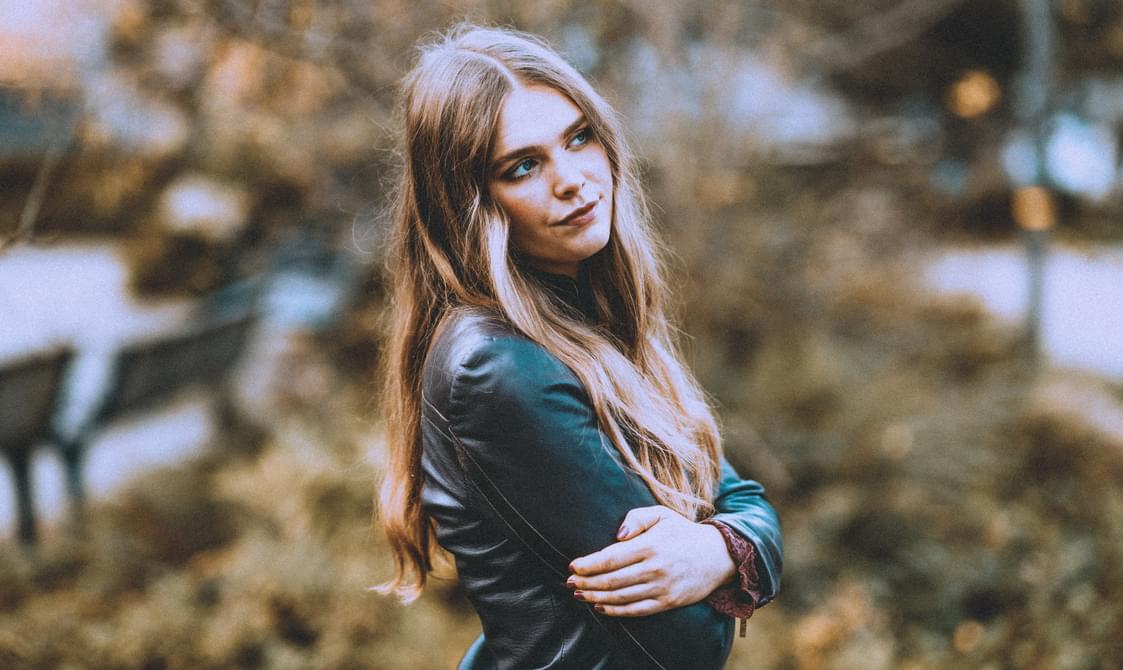 young woman with long fair hair and arms folded, looking away from the camera.