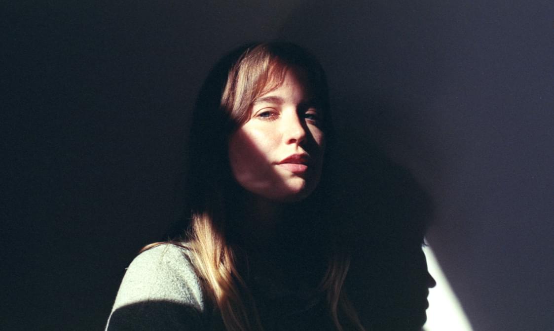 Young woman with long blonde hair, face partially in shadow.