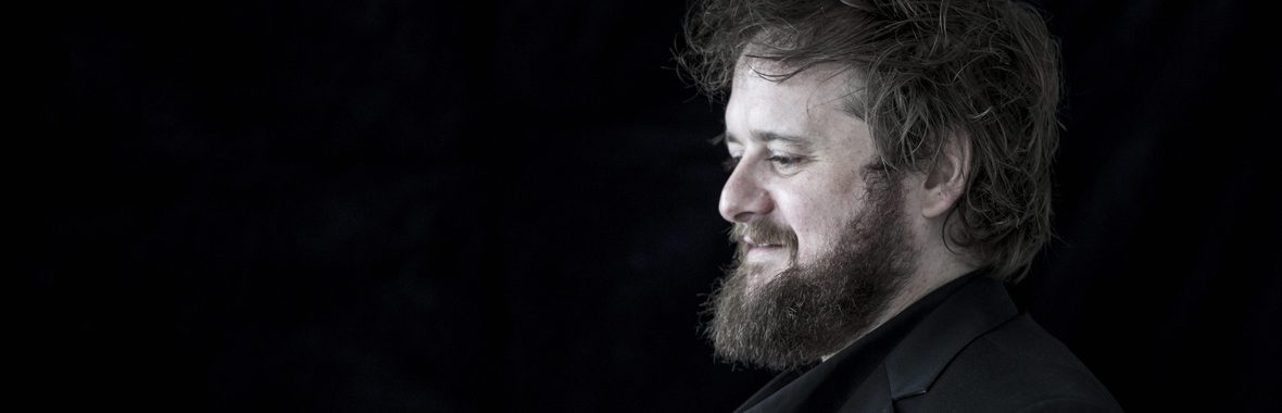 Black and white image of Allan Clayton, man with dark hair and beard facing sideways.