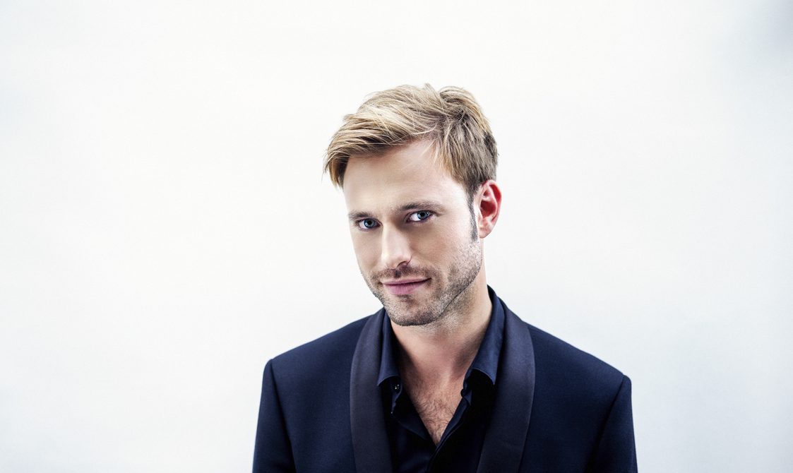 Blond man wearing a dark jacket looking into the camera.
