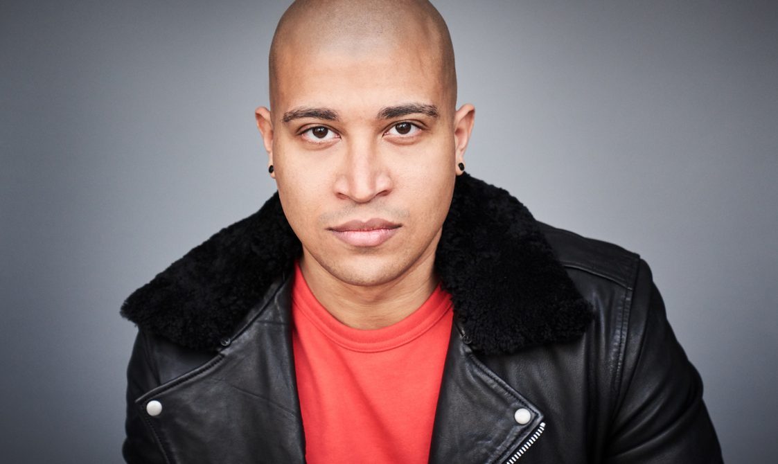 Man in red tshirt and leather jacket looking intensely into the camera.