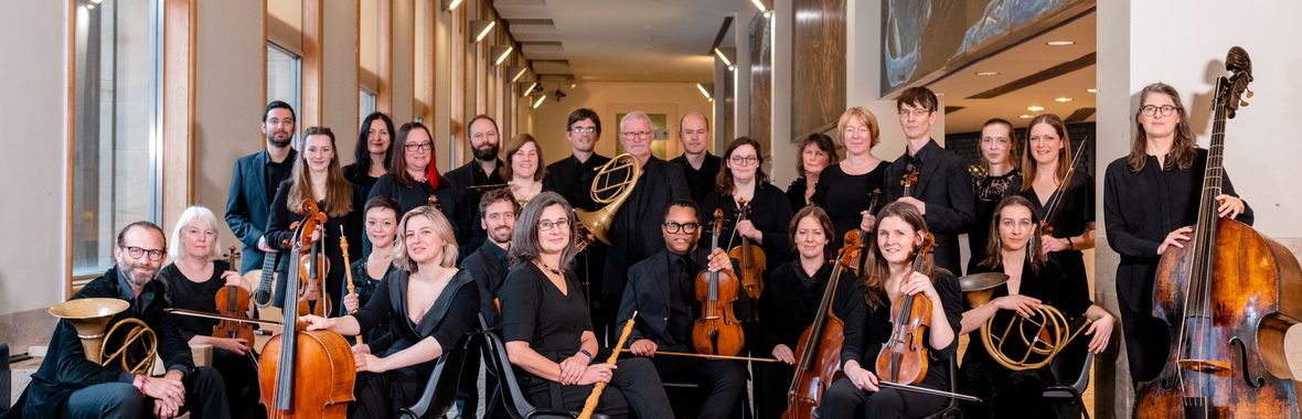 Dunedin Consort musicians sitting and standing in a gallery with their instruments.