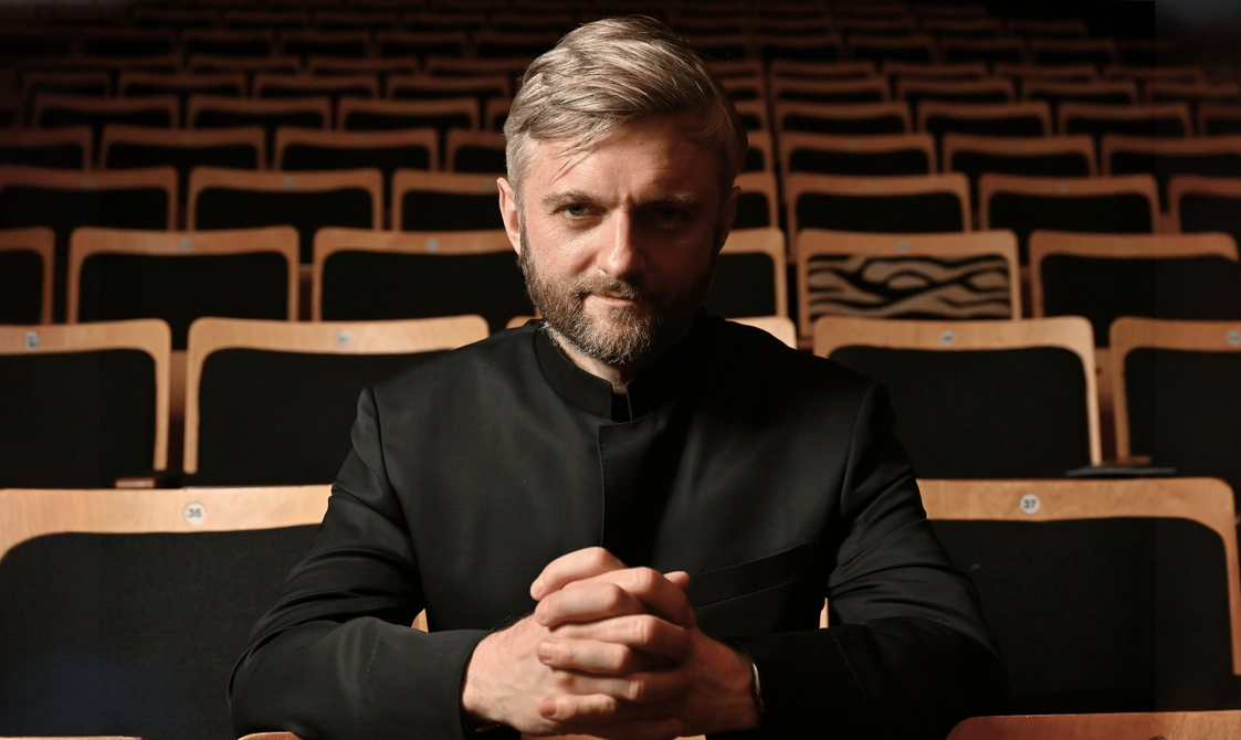 Close-up of a man with silvery hair sitting in a concert hall and looking into the camera