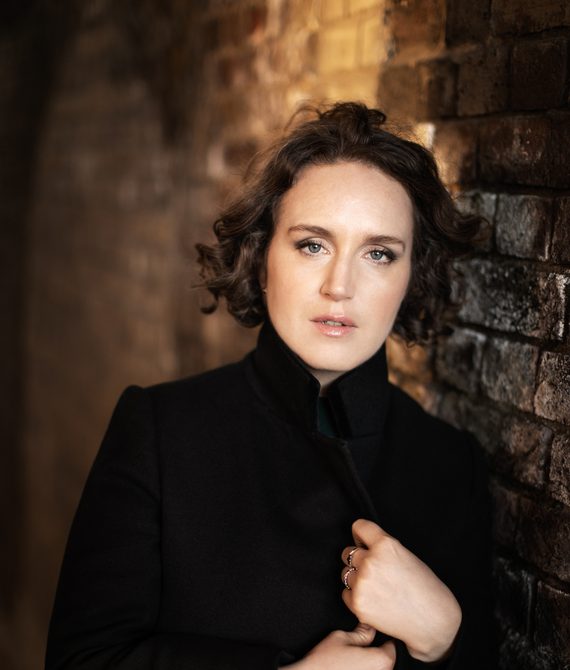 Woman with dark hair wearing black standing next to a brick wall