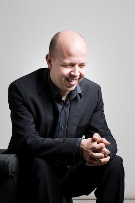Man wearing a dark suit, sitting and smiling.