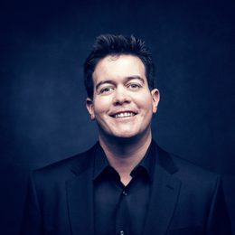 Man with short dark hair wearing a dark jacket and smiling into the camera.