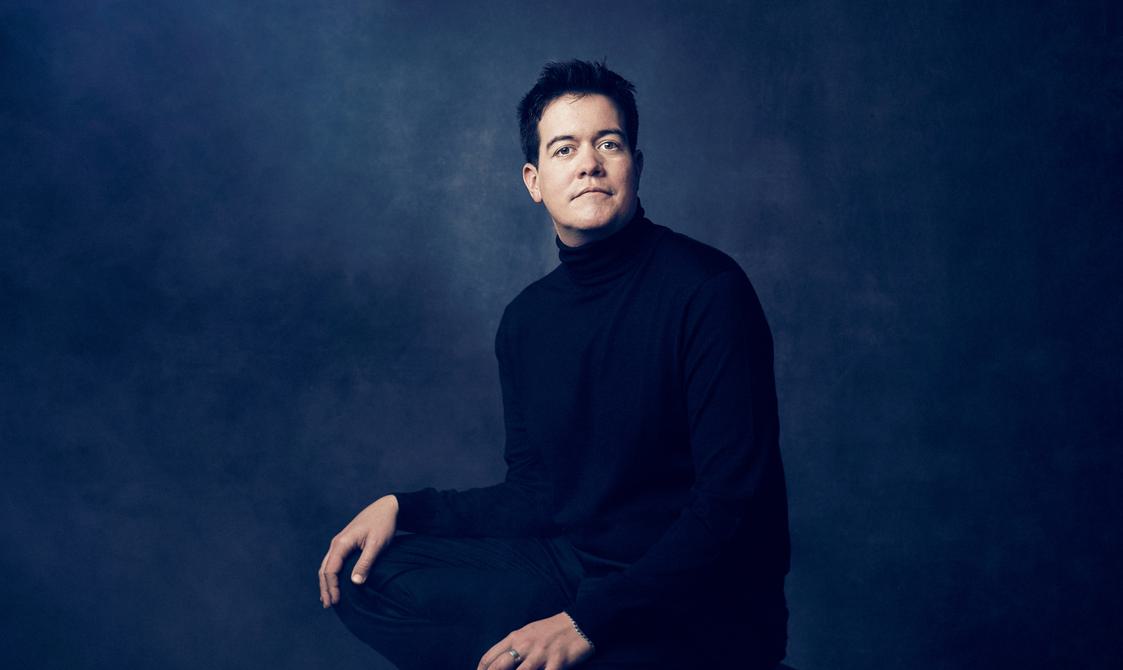Man with dark hair wearing a dark sweater looking at the camera.