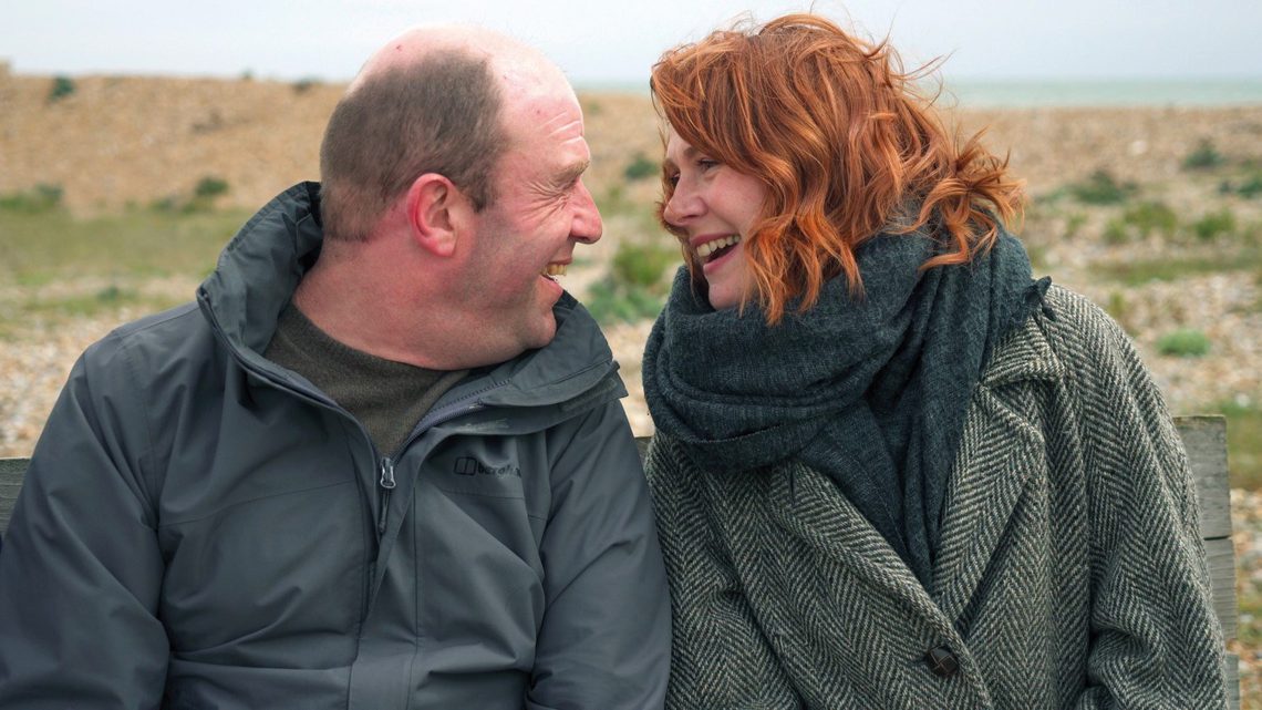 Man and woman sitting together on a beach facing each other and smiling.