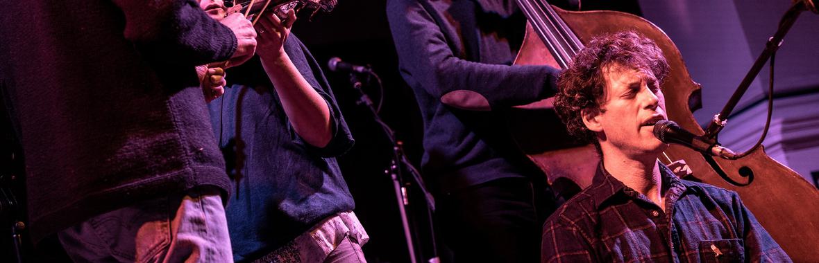 Man with short brown hair onstage singing into a microphone