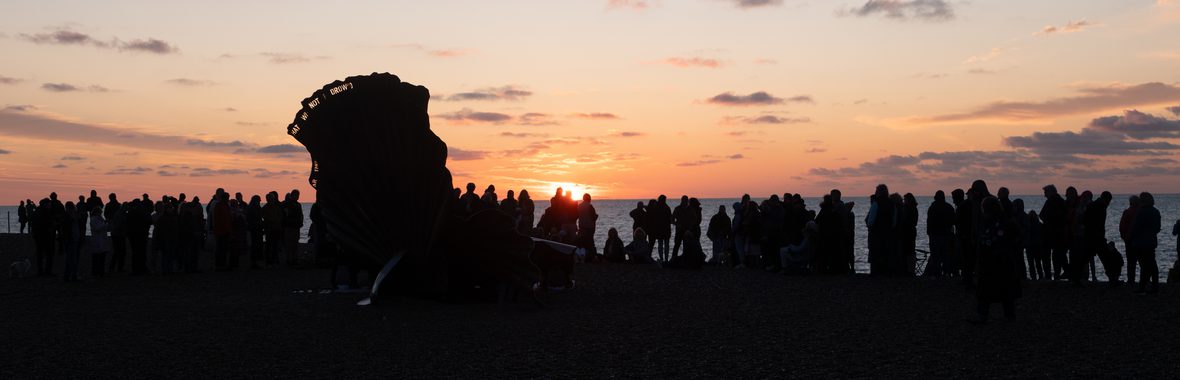 Crowd of people in silhouette standing on the beach and watching the sunrise over the sea