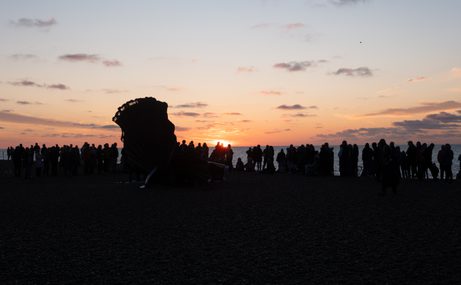 Crowd of people in silhouette standing on the beach and watching the sunrise over the sea