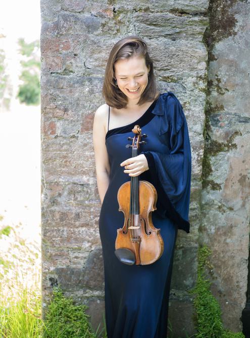 Woman standing outside wearing a blue dress and holding a violin.