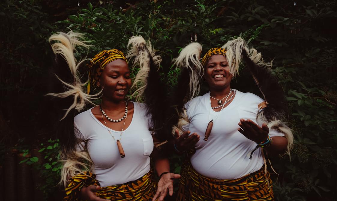 Two women wearing white tshirts and wearing African headdresses.