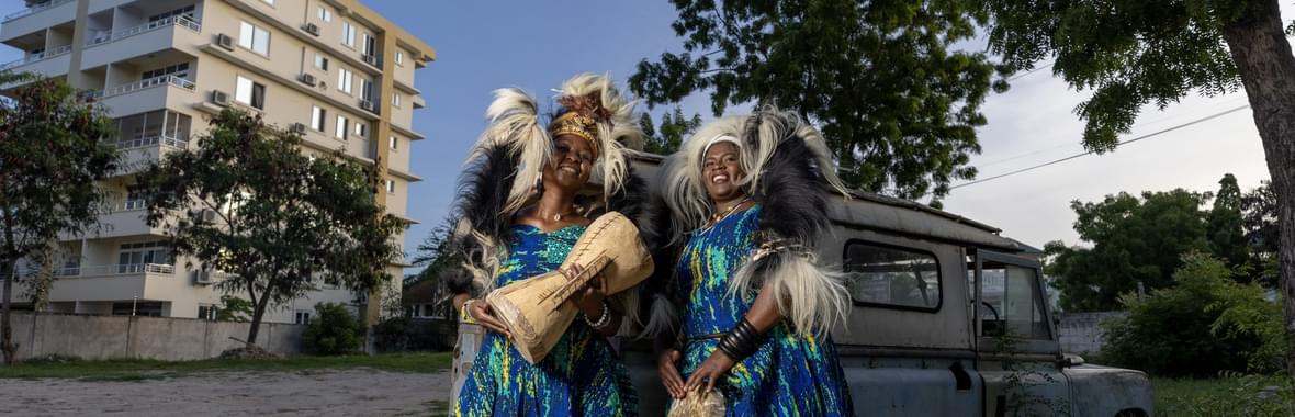 Two women wearing brightly coloured dresses and African headdresses.