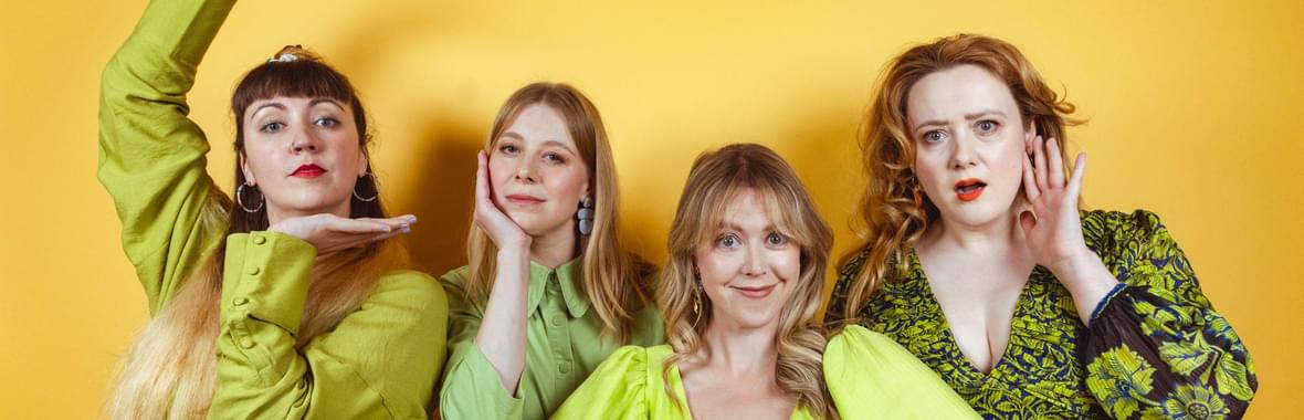 Four women wearing green dresses, making poses and smiling.