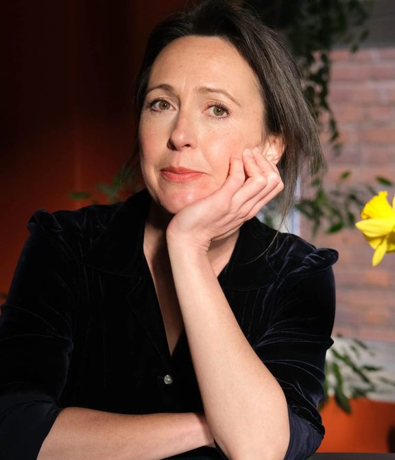 Woman with hair tied back, wearing a black top and looking at the camera