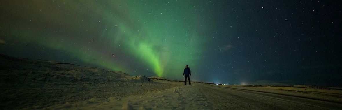 Solitary figure standing under the northern lights.