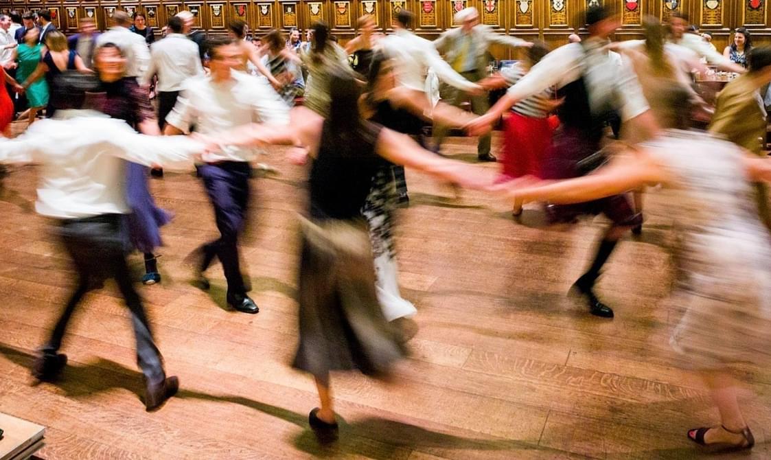 Blurred image of dancers holding hands whilst dancing around a hall.