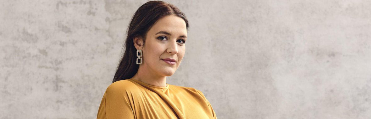 Woman with long dark hair, wearing a yellow dress and long, sparkly earrings.