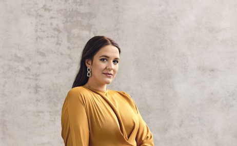 Woman with long dark hair, wearing a yellow dress and long, sparkly earrings.