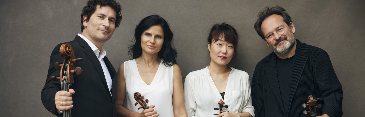Two men and two women holding their instruments and standing together against a grey background.