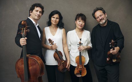 Two men and two women holding their instruments and standing together against a grey background.