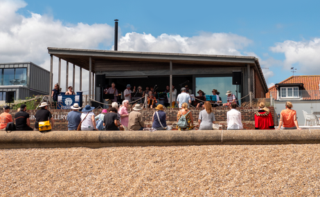 Group of people on a stage being watched by an audience from the beach.