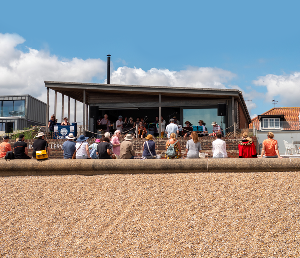 Group of people on a stage being watched by an audience from the beach.