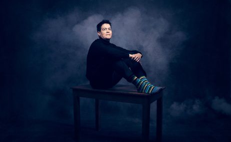 Man with short black hair sitting with his hands folded in front of him.