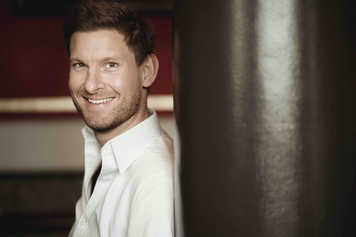 Main with short hair wearing a white shirt and smiling.