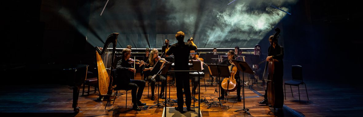 Silhouetted small orchestra with smoke and lighting in the background.
