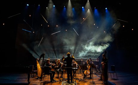 Silhouetted small orchestra with smoke and lighting in the background.