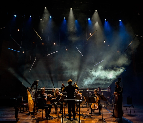 Silhouetted small orchestra with smoke and lighting in the background.