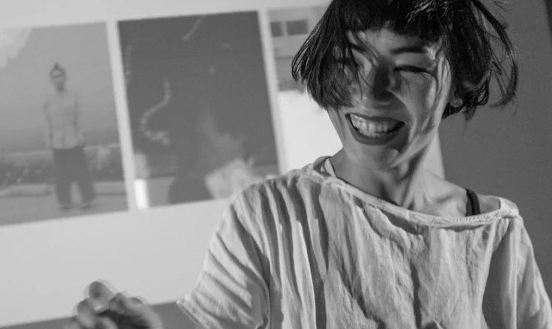 black and white picture of a woman with short black hair laughing against a background of wall art.
