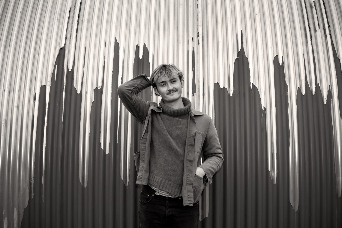 Blond young man standing against a corrugated iron wall.