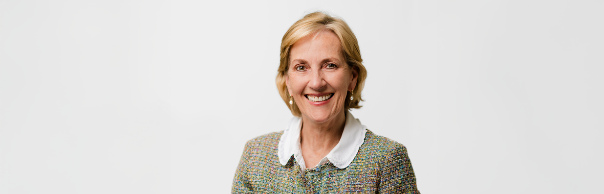 Woman with short blonde hair wearing a patterned jacket and blouse, smiling.